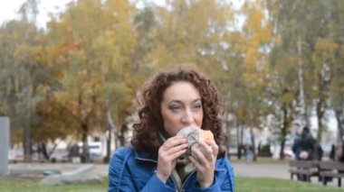 Öğrenci kız parkta hamburger ya da çizburger yiyor.