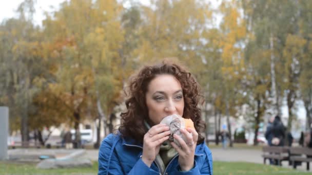 Estudante menina comer um hambúrguer ou cheeseburger em um parque — Vídeo de Stock