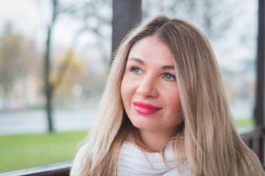 Güzel sarışın kız portresi, sokakta beyaz bir kazak içinde.