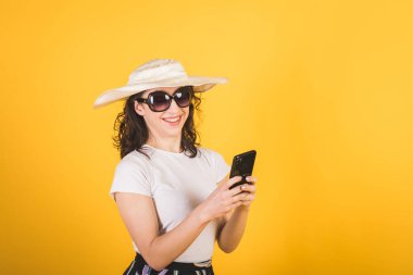 Güneş gözlüklü güzel bir kız ve sarı arka planda telefonu olan büyük beyaz bir şapka.