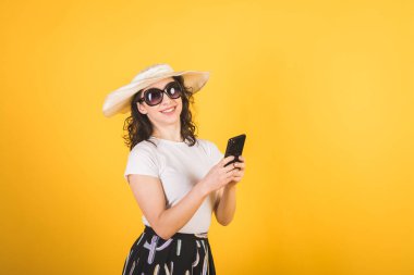 Güneş gözlüklü güzel bir kız ve sarı arka planda telefonu olan büyük beyaz bir şapka.
