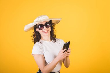 Güneş gözlüklü güzel bir kız ve sarı arka planda telefonu olan büyük beyaz bir şapka.