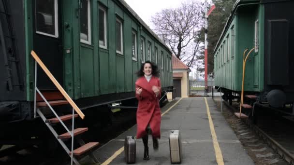 Vídeo engraçado, uma mulher de casaco vermelho e duas malas está dançando na plataforma da antiga estação ferroviária — Vídeo de Stock