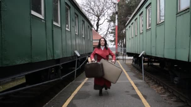 Забавное видео, женщина с чемоданами в красном пальто танцует на старинной железнодорожной платформе — стоковое видео