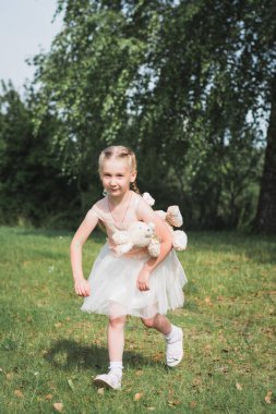 Oyuncak ayıyla küçük kız yaz parkında eğleniyor.