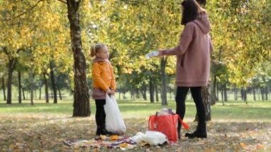Anne ve küçük kızı parkta bir şeyler topluyorlar.