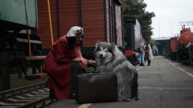 Kırmızı paltolu bir kadın ve büyük bir köpek platformda treni bekliyor.