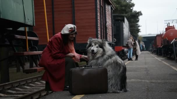 En kvinna i röd rock och en stor hund väntar på tåget på perrongen — Stockvideo
