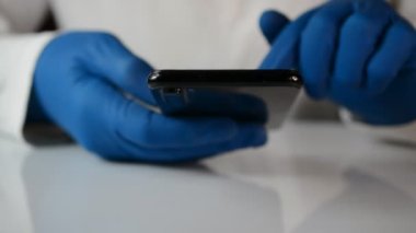 Mavi eldivenli doktor siyah bir telefona mesaj yazıyor.
