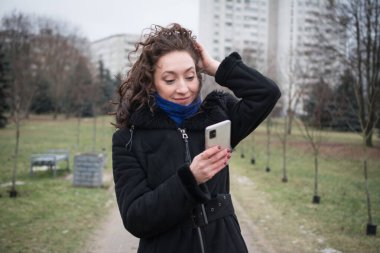 Sıcak giysiler içinde güzel bir kız bulutlu bir kış gününde şehrinin etrafında yürüyor.