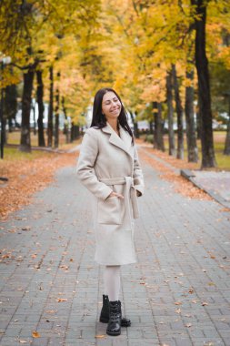 Sonbaharda şehir parkında yürüyen zarif esmer kız.