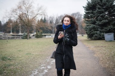 Sıcak giysiler içinde güzel bir kız bulutlu bir kış gününde şehrinin etrafında yürüyor.