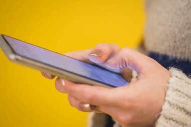 Kadın eli ve telefonu sarı arkaplanda.