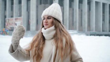 Genç bir kadın akıllı telefondan arkadaşıyla görüntülü sohbet ederken gülümsüyor.