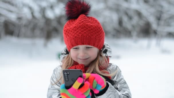 Pequeno retrato de menina caucasiana no parque de inverno escreve uma mensagem em um smartphone — Vídeo de Stock