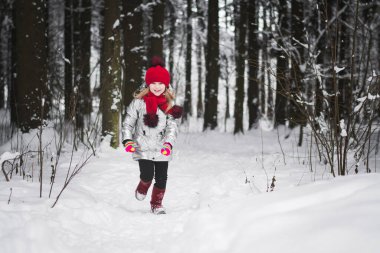 Küçük mutlu kız kışın karlı bir ormanda eğleniyor.