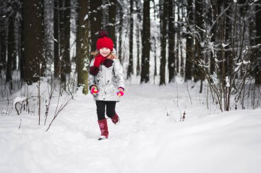 Küçük mutlu kız kışın karlı bir ormanda eğleniyor.