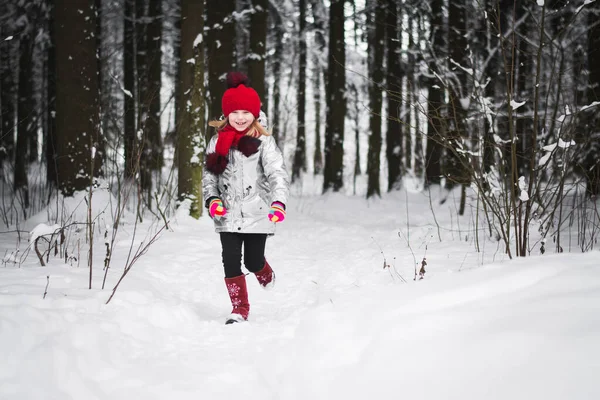 Küçük mutlu kız kışın karlı bir ormanda eğleniyor.