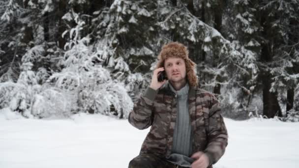 Zabawny portret młodego człowieka w śnieżnym lesie rozmawiający przez telefon — Wideo stockowe