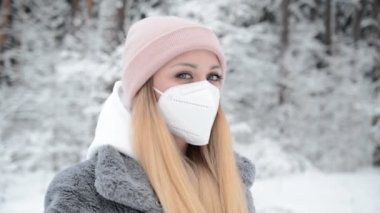 Kışın karlı bir ormanda, koruyucu bir maske takmış sarışın bir kızın portresi.
