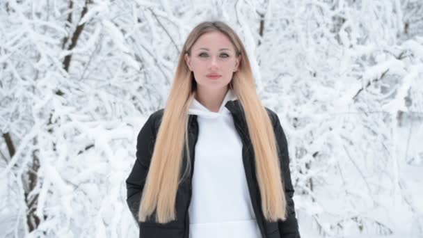 Mooi stijlvol blond meisje met lang haar staat in een besneeuwd bos — Stockvideo