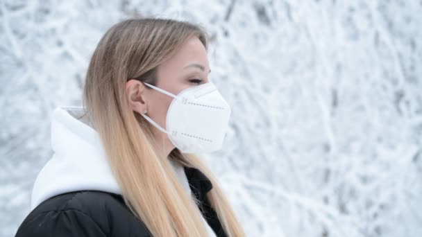 Portret van een mooie jonge vrouw vrouw met medisch gezichtsmasker buitenshuis in besneeuwd winterbos — Stockvideo