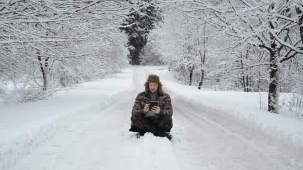 Guy wandelaar zit op de weg in de winter met een tablet — Stockvideo