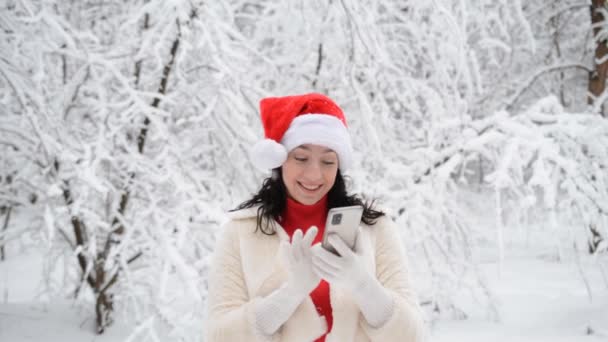 Vacker flicka i vinter kläder av röda och vita färger ler och skriver ett meddelande på sin telefon — Stockvideo