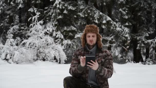 Wandelaar met tablet in handen in de winter in besneeuwd bos — Stockvideo