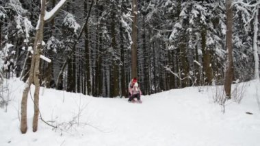 İki mutlu güzel çocuk karla kaplı bir ormanda kızak gezintisi yapıyor.