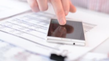 İş adamı mali raporları kontrol eder ve telefondaki numaraları sayar.