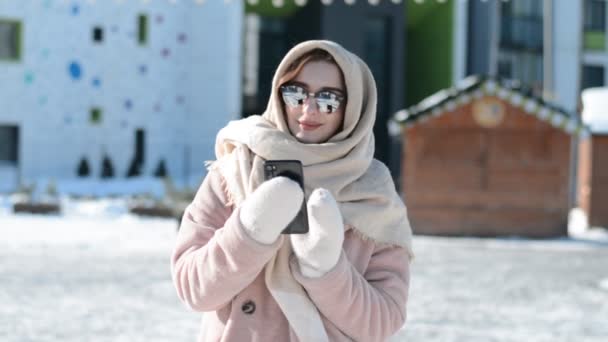 Een prachtig Russisch meisje in de winter op een ijzige zonnige dag tegen de achtergrond van moderne stedelijke gebouwen — Stockvideo