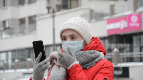 Adolescente mujer joven con una máscara facial durante la pandemia de Coronavirus COVID-19 usando su teléfono inteligente o celular para redes sociales fuera — Vídeo de stock