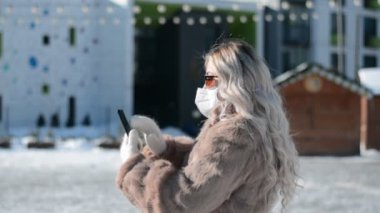 Maskeli ve elinde telefon olan şık bir kızın yan görüntüsü bir mesaj yazar.