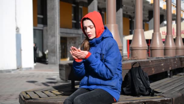 Krásná hipster dívka sedí na lavičce ve městě a zamrzá — Stock video