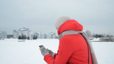 Kışın elinde telefon olan yalnız bir kızın arkası.