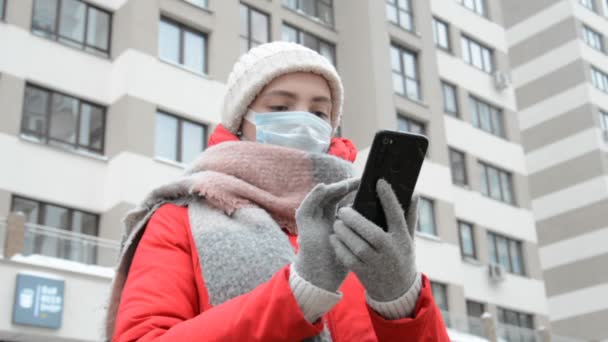 Dziewczyna w masce ochronnej i rękawiczki za pomocą czarnego smartfona — Wideo stockowe