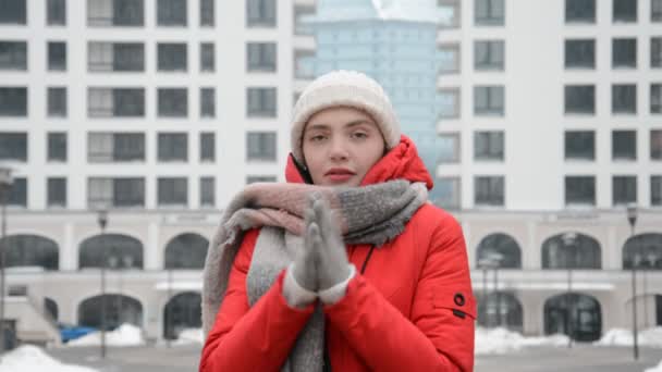 Egy vörös kabátos lány portréja a városban, a modern épületek hátterében egy erős hideg ősszel, télen vagy tavasszal — Stock videók