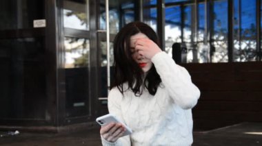 Şehirde kırmızı dudakları olan, beyaz, esmer bir kadının portresi cep telefonundan dinleniyor.