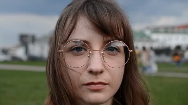在多云的天空中，一个戴着眼镜、年轻美丽的棕色头发女孩严肃的脸 — 图库视频影像