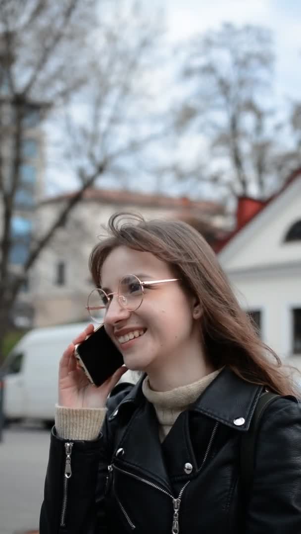 Молодая красивая девушка в очках улыбается и разговаривает по телефону — стоковое видео