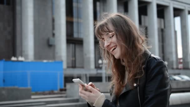 Porträt einer lächelnden jungen kaukasischen Frau, die ihr Smartphone in der Hand hält, lustige Nachrichten liest und mit Freunden chattet — Stockvideo