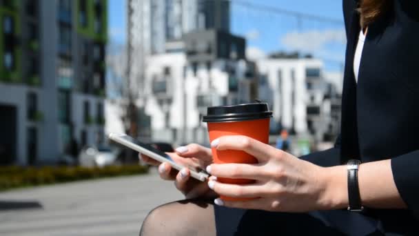 Caucasian business woman with smartphone and cup of coffee in hands outdoors — Stock Video