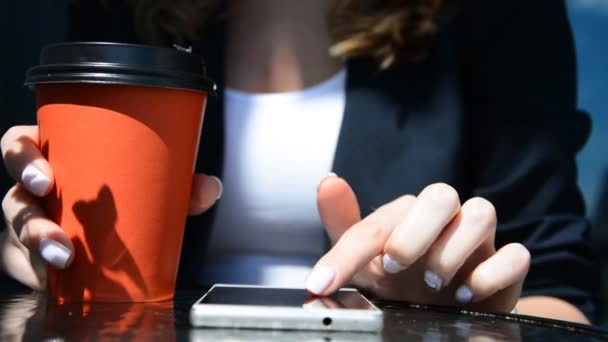 Primer plano de hermosas manos femeninas de negocios jóvenes desplazándose teléfono inteligente en la cafetería con taza de café — Vídeo de stock