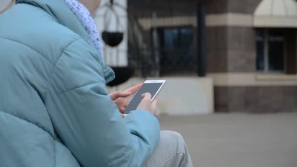 Een meisje typt een bericht op de smartphone zitten tegen — Stockvideo