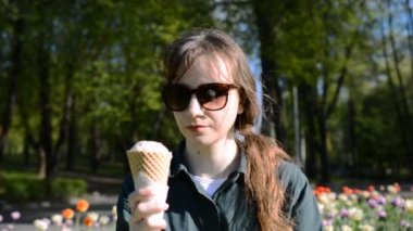 Güzel genç bir kadın parkta yeşil bir çimenlikte oturuyor ve dondurma yiyor.