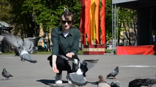 Una giovane ragazza caucasica nutre piccioni per la strada della sua città in una giornata estiva soleggiata — Video Stock