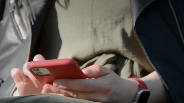 Крупним планом молода жінка набирає смс прокрутки фотографій на червоному телефоні — стокове відео