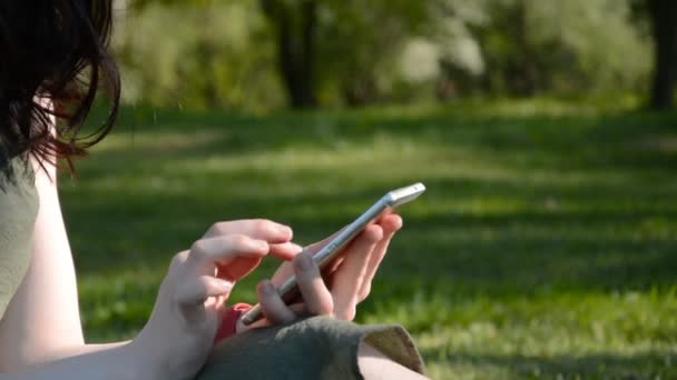 Mujer joven mensajes de texto en el teléfono inteligente sentado en el parque de la ciudad — Vídeos de Stock