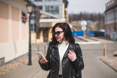 Güneşli bir bahar gününde, elinde telefonla caddede yürüyen güzel bir hippi kız.
